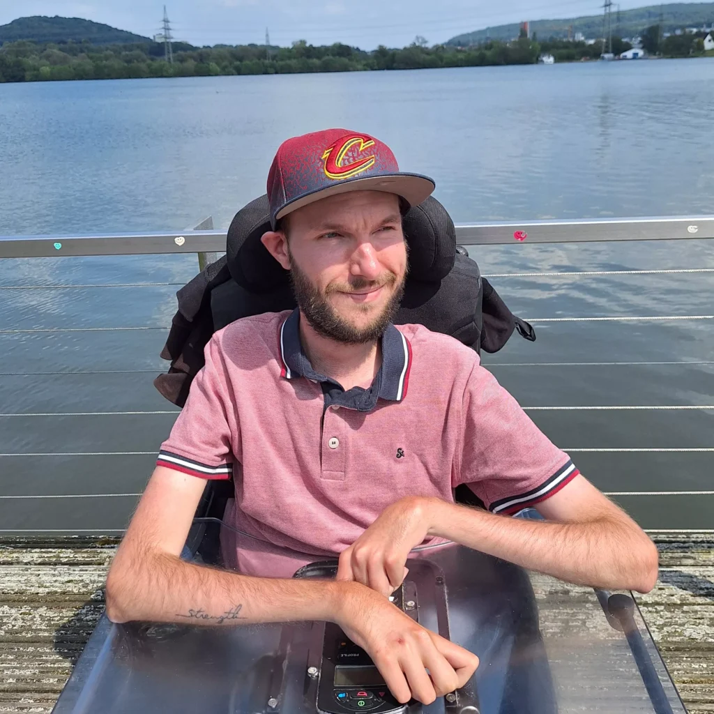 Portrait vom Autor Matthias Pelka. Er sitzt in einem Rollstuhl, trägt ein Basecap und ein T-Shirt. Im Hintergrund ist ein See zu sehen.